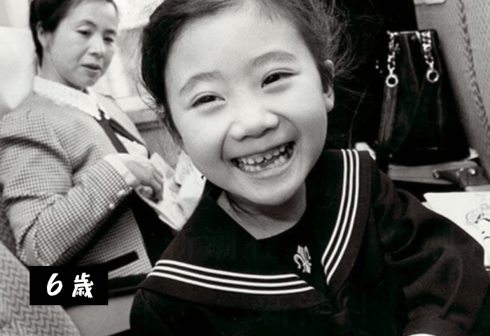 元卓球選手福原愛さんの6歳の時の画像（白黒写真）
新幹線の車内
幼稚園年長さんで可愛い制服を着用
笑顔を振りまいている
後ろに福原千代さん（愛さんのお母さん）が写っている